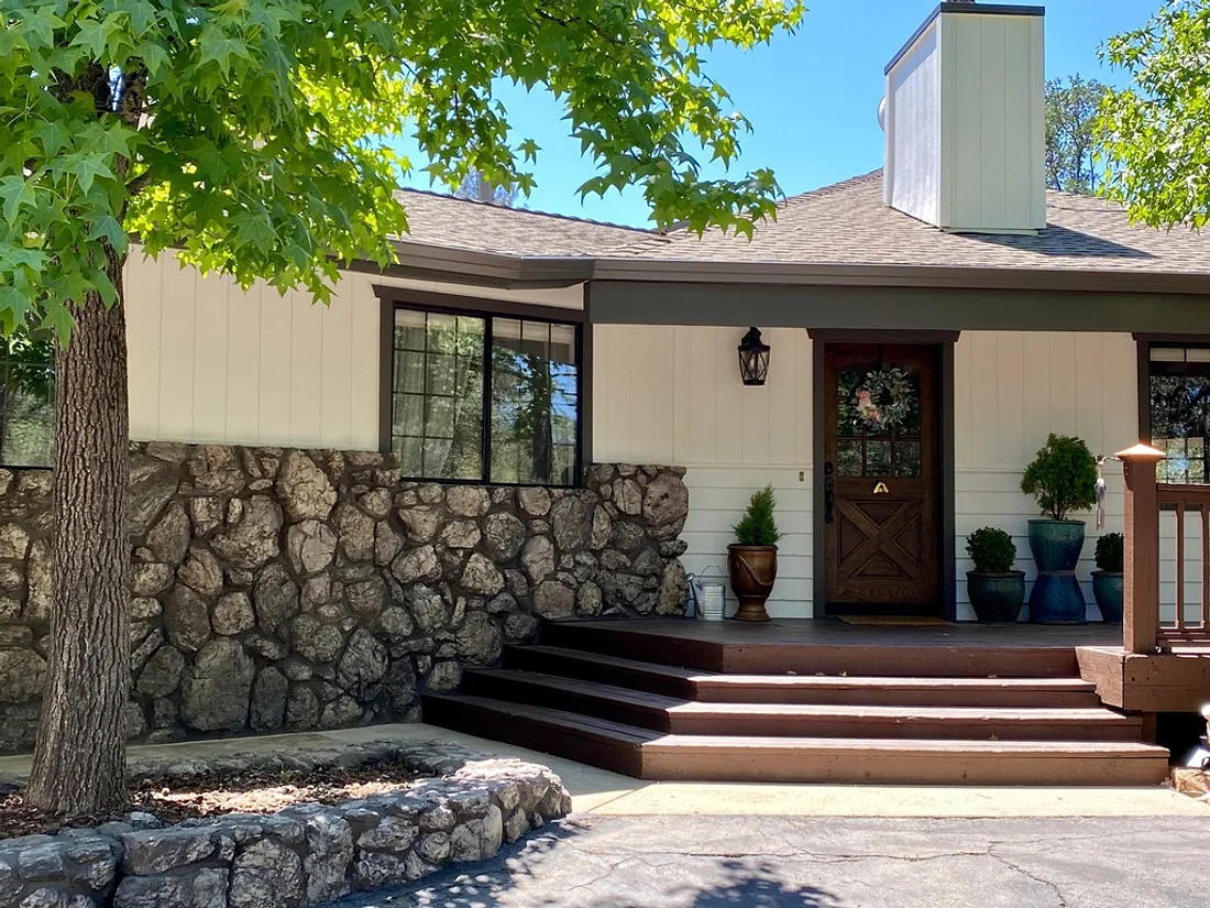 Home exterior painted in warm cream with dark brown trim above a stone base
